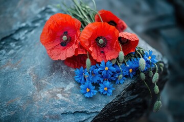 Obraz premium Vibrant wildflowers on stone: Poppies and cornflowers create a striking floral display for design and nature enthusiasts.