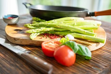 Green asparagus and ingredients for roasting in a pan. Fresh local  vegetables and a cast iron pan on a wooden cutting board. Preparing and cooking for healthy eating.