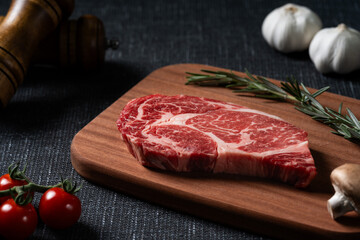 A fresh steak with rosemary, tomato, mushroom and garlic is placed on a wooden plate