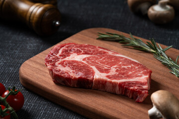 A fresh steak with rosemary, tomato, mushroom and garlic is placed on a wooden plate