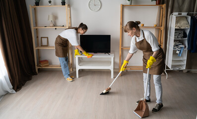 Two female janitors cleaning home wiping dust and sweeping in the living room. Concept of cleaning...
