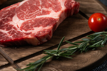 A fresh steak with rosemary, tomato, mushroom and garlic is placed on a wooden plate