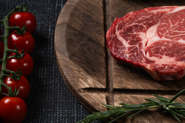 A fresh steak with rosemary, tomato, mushroom and garlic is placed on a wooden plate