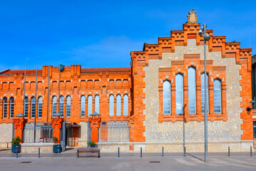 Rovira i Virgili University in Tarragona city from Catalonia Spain. Striking red brick building with arched windows and ornate stonework, set against blue sky with a bench and streetlamp in foreground