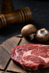 A fresh steak with rosemary, tomato, mushroom and garlic is placed on a wooden plate