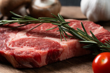 A fresh steak with rosemary, tomato, mushroom and garlic is placed on a wooden plate