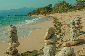 Stone cairns stand on a sandy beach, providing a tranquil contrast to the gentle waves and distant...