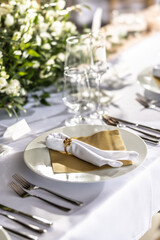 A wedding table covered with a white tablecloth, decorated with flowers, candles, glasses and cutlery