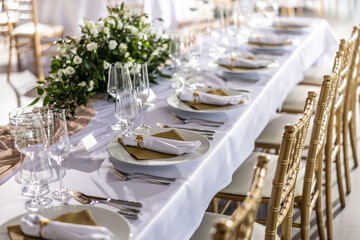 A wedding table covered with a white tablecloth, decorated with flowers, candles, glasses and cutlery