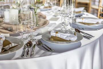 A wedding table covered with a white tablecloth, decorated with flowers, candles, glasses and cutlery