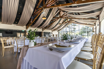 Wedding setting and decorated tables in a beautiful modern interior of a performance hall with a modern light ceiling of wooden construction