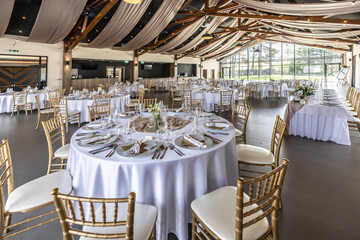 Wedding setting and decorated tables in a beautiful modern interior of a performance hall with a modern light ceiling of wooden construction