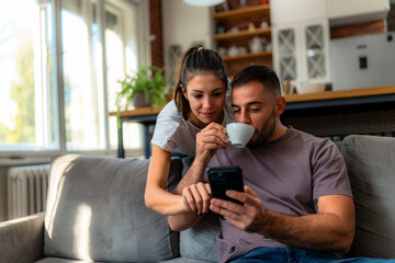 Couple relaxes on gray couch, sipping coffee and excitedly searching for their next vacation...