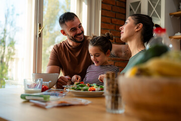 Portrait of a joyful family - parents and child - gathered around the kitchen table during their...
