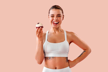 Beautiful sporty girl holds a small low-calorie dessert, winks, and runs her tongue over her teeth...