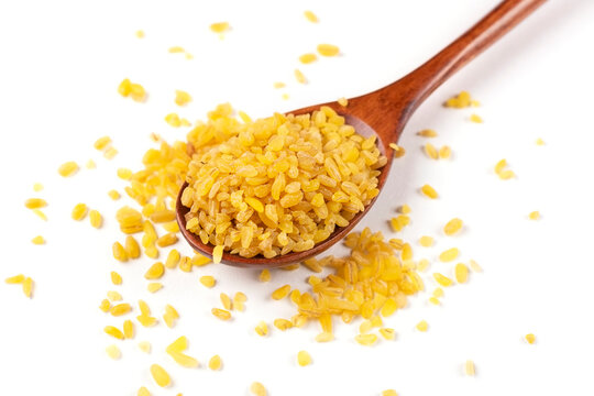 A handful of bulgur groats in a brown wooden spoon in close-up on a white isolated background.