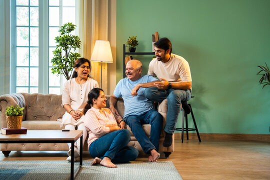 Laughing together while sitting indoors, cheerful Indian family enjoying quality time on sofa