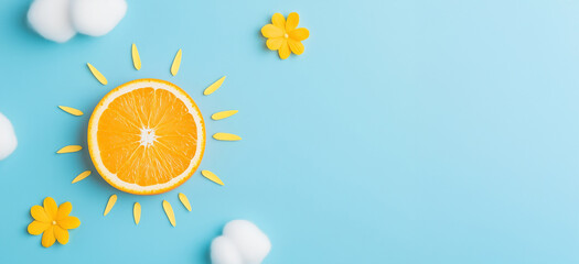 Orange slice as sun with white cotton clouds on blue background. Vitamin C and cosmetic concept. Image for skincare, health products, social media banner and advertisement with copy space.