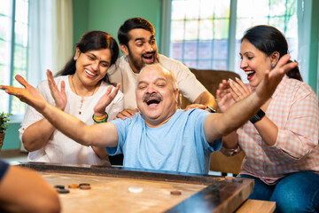 Playing indoor carrom tabletop game, Indian family bonds over fun moments in living room