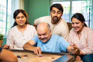 Playing indoor carrom tabletop game, Indian family bonds over fun moments in living room