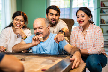 Playing indoor carrom tabletop game, Indian family bonds over fun moments in living room