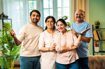 Smiling at camera, Indian family of four standing together in cozy and modern living room