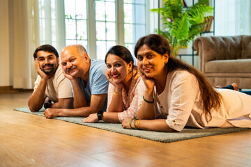 Lying together and smiling, Indian parents with grownup kids pose happily on cozy home floor