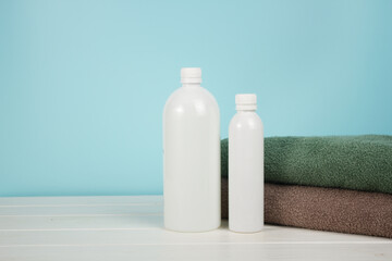 Empty bottles of shampoo and shower gel with towels on blue background.