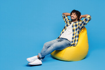 Full body young smiling Indian man he wear yellow checkered shirt casual clothes sit in bag chair...