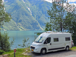 A picturesque camper van parked near the tranquil shores of a Norwegian fjord, surrounded by...