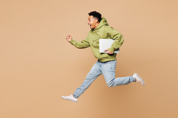 Full body young IT man of African American ethnicity wears green hoodie casual clothes jump high...