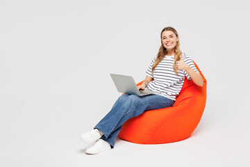 Full body young IT woman she wear striped t-shirt casual clothes sit in bag chair hold use work on...