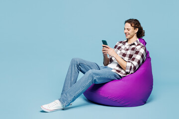 Full body young man he wear purple checkered shirt casual clothes sit in bag chair hold in hand use...