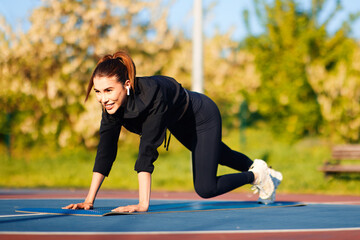 Happy athlete listening music with wireless earphones and training doing mountain climber exercise on fitness mat in a park