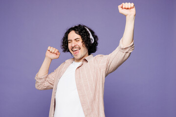 Young fun brunet man he wears pink shirt t-shirt casual clothes listen to music in headphones raise...