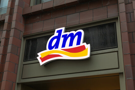 A brightly lit dm (drogerie markt) logo sign on a building facade indicates a retail drugstore in a European city. Berlin, Germany. 29 March 2025.