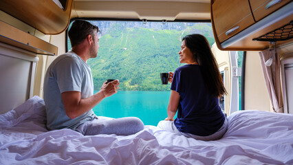 A couple relaxes inside their camper van, sipping coffee while admiring the breathtaking fjord...