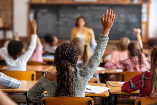 Young girls and boys in an elementary school setting are raising their hands in a classroom