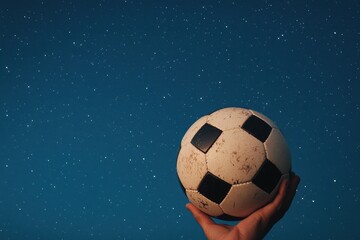 Naklejka premium Hand Holding Soccer Ball Against Starry Night Sky Background