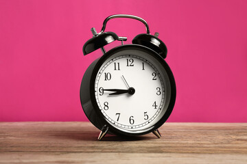 One black alarm clock on wooden table against bright pink background