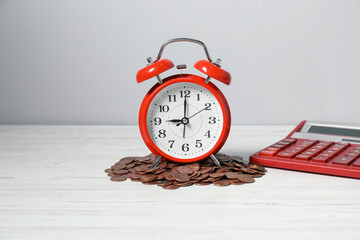 Alarm clock, coins and calculator on white wooden table. Tax time