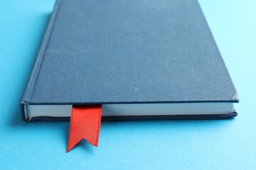 Book with red ribbon bookmark on light blue background, closeup