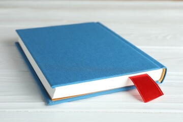 Book with red ribbon bookmark on white wooden table, closeup