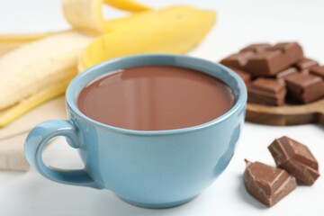 Tasty chocolate milk in cup, pieces and banana on white table, closeup