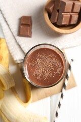 Tasty chocolate milk in glass, banana and pieces on white wooden table, flat lay