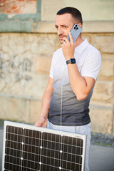 Handsome man using smartphone connected to photovoltaic solar panel. Integration of sustainable...
