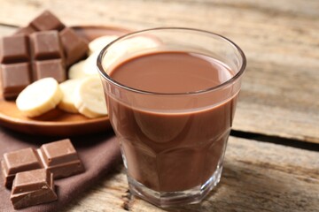 Tasty chocolate milk, pieces and banana on wooden table, closeup