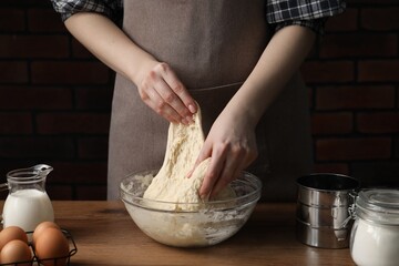 Woman kneading raw dough at wooden table, closeup