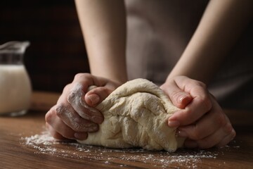 Woman kneading raw dough at wooden table, closeup