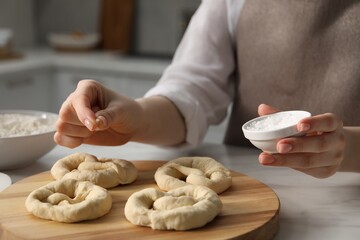 Woman adding sea salt onto uncooked pretzels at table indoors, closeup